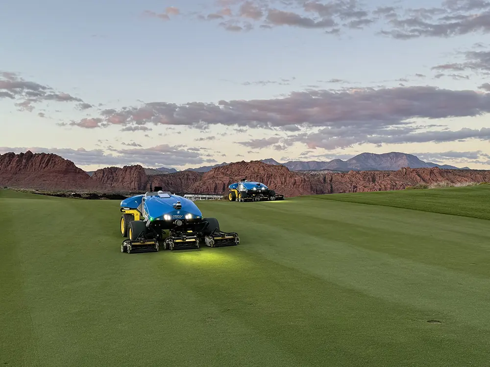 Two autonomous reel mowers on a golf fairway with red-rock scenery beyond