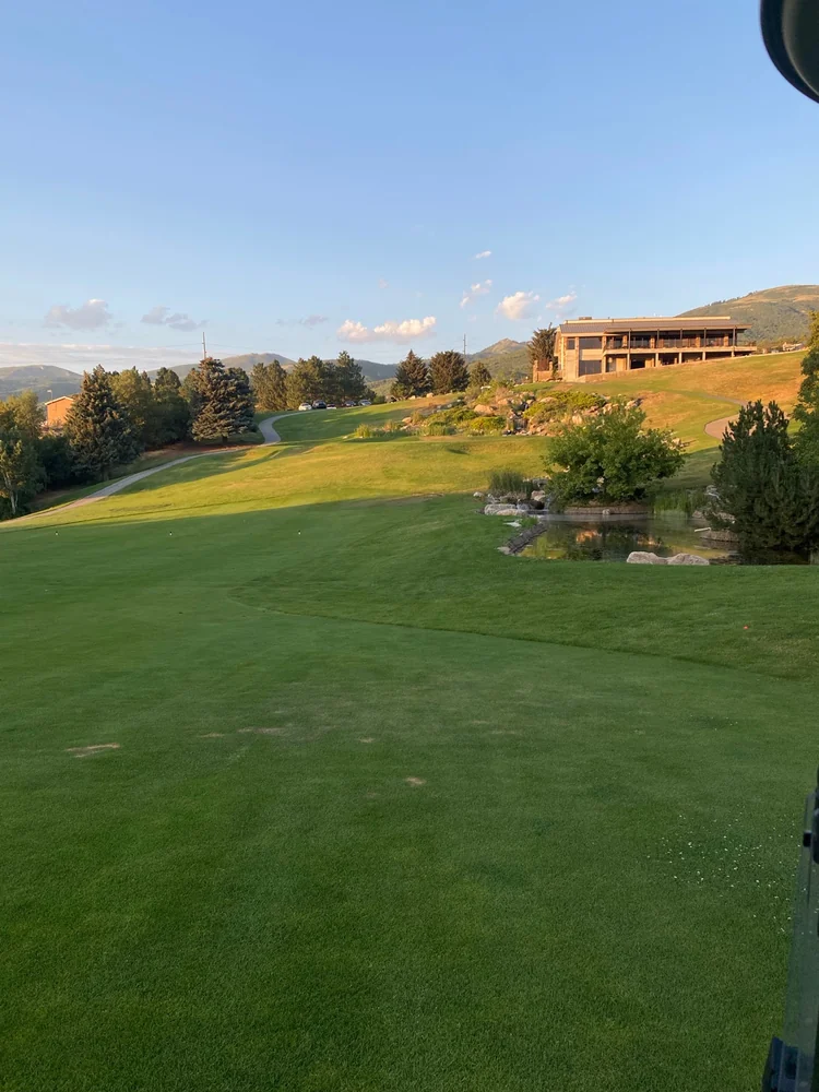 Grass, a pond and trees below a hillside building at Bountiful Ridge Golf Course.