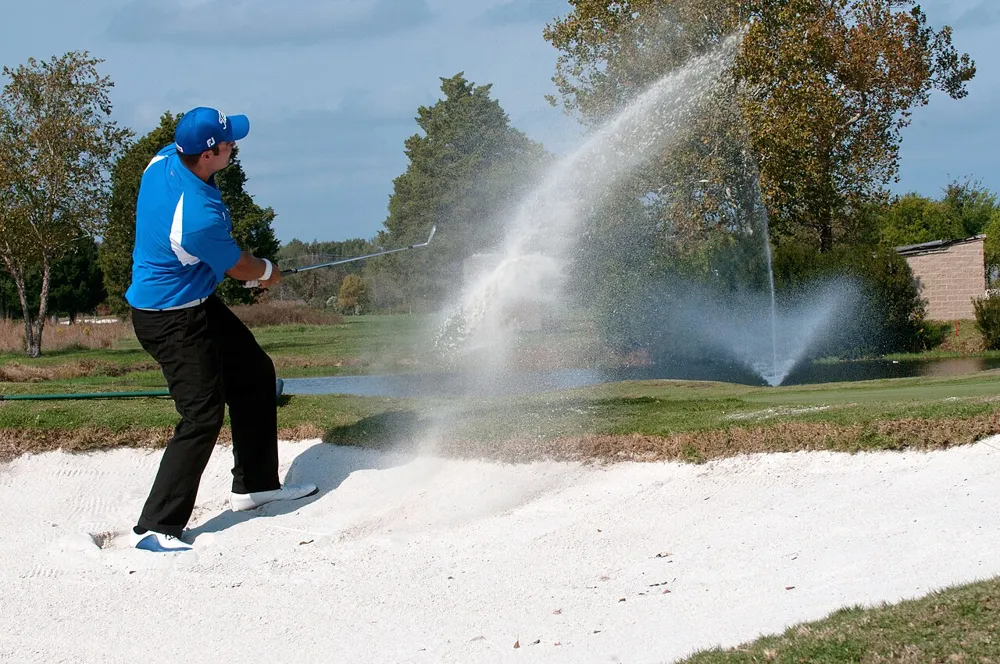 A golfer in a sand bunker at Eaglewood Golf Course swinging toward the green
