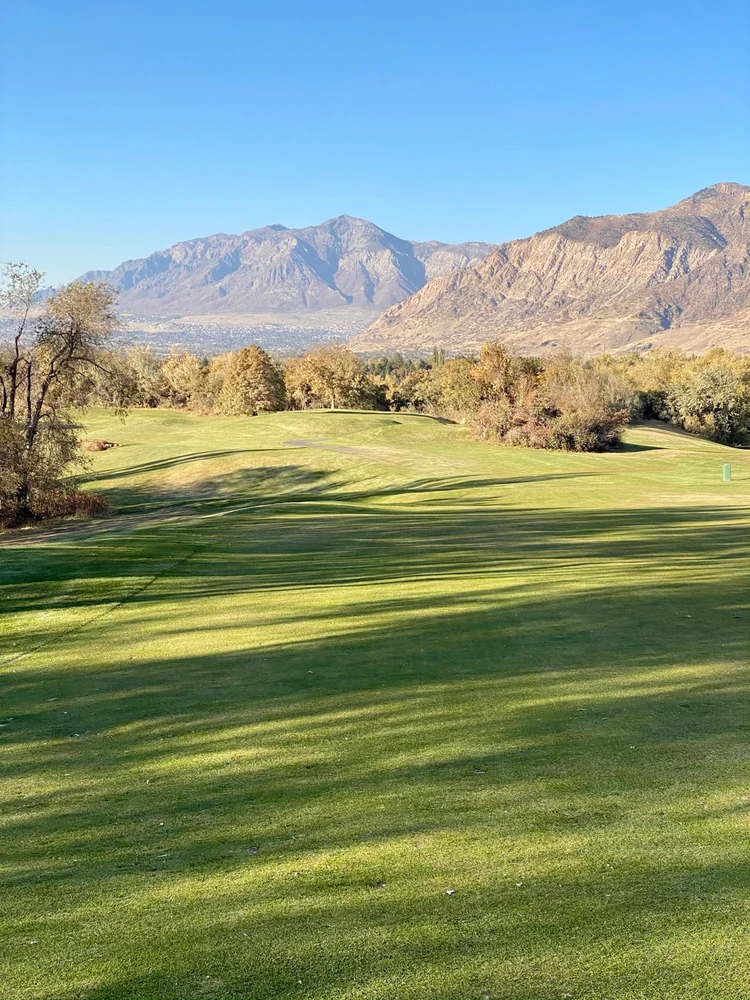 Tree-lined fairways and cart paths at Mount Ogden Golf Course beneath rocky mountain slopes.