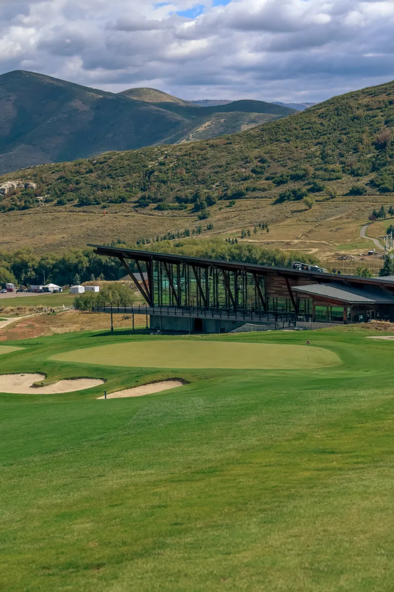 The Soldier Hollow clubhouse beyond a green, with mountains and clouds behind.