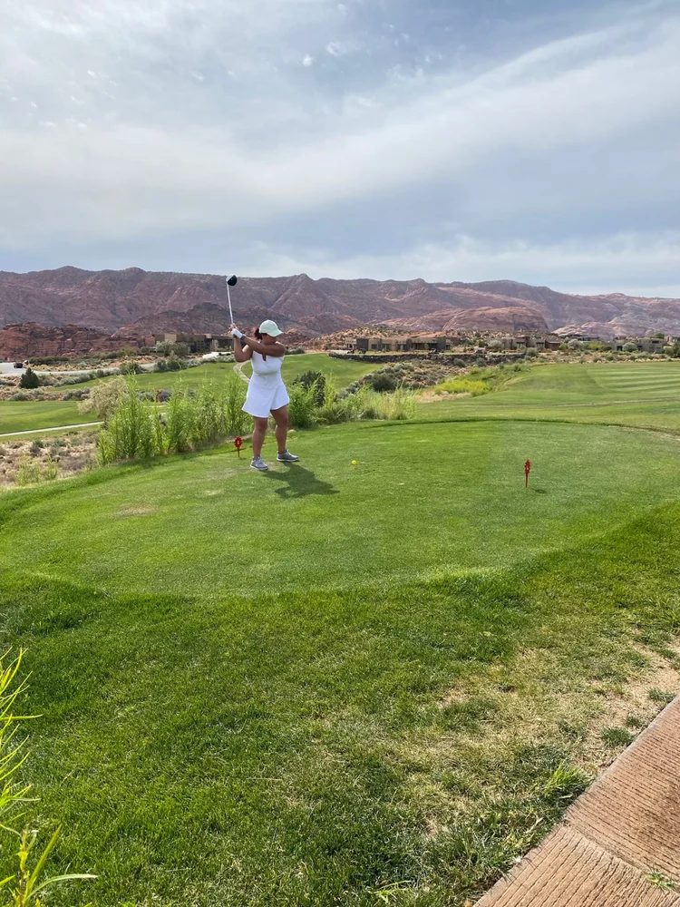 A golfer swinging from a tee at The Ledges, with fairways and red rock cliffs beyond.