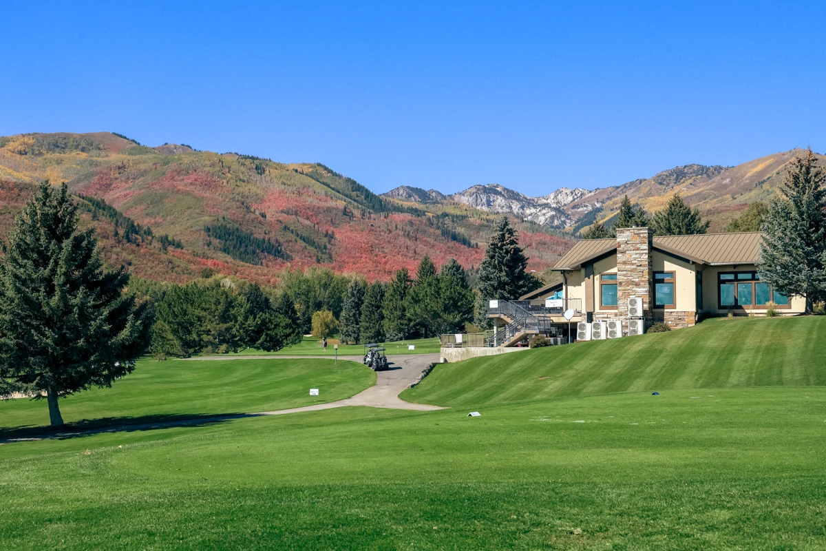 The Wasatch Mountain Golf Course clubhouse above a green fairway, with autumn hills beyond.