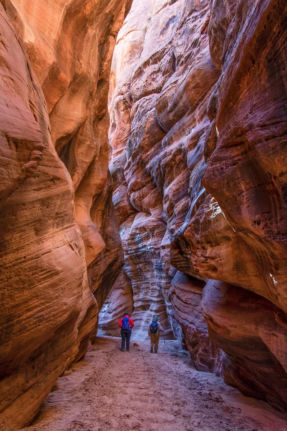 Two hikers walking between tall red sandstone walls in Buckskin Gulch
