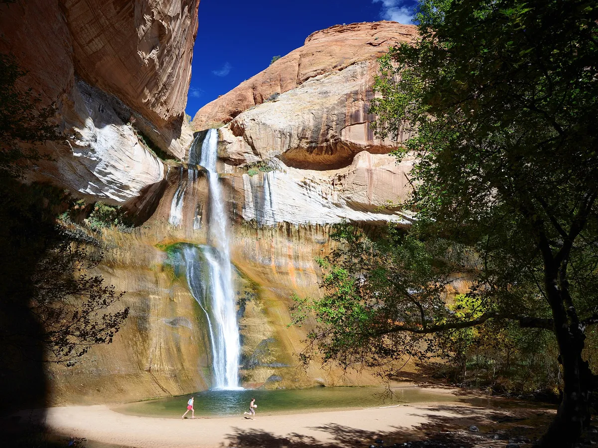 Lower Calf Creek Falls dropping into a sandy pool below red sandstone cliffs