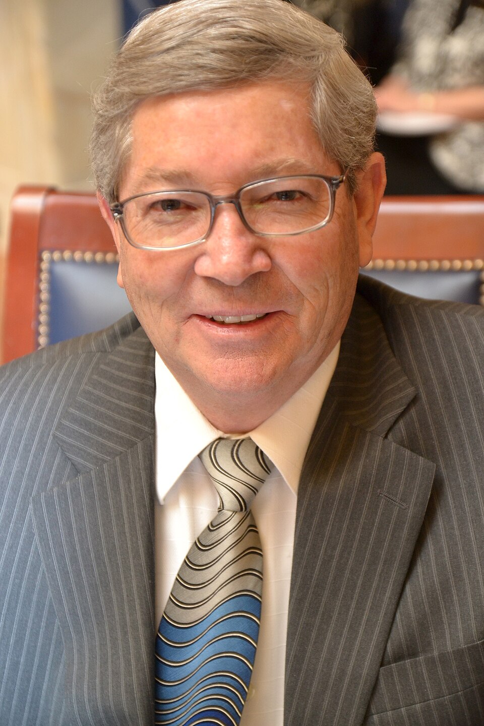 David Hinkins smiling in glasses, a gray suit and patterned tie.