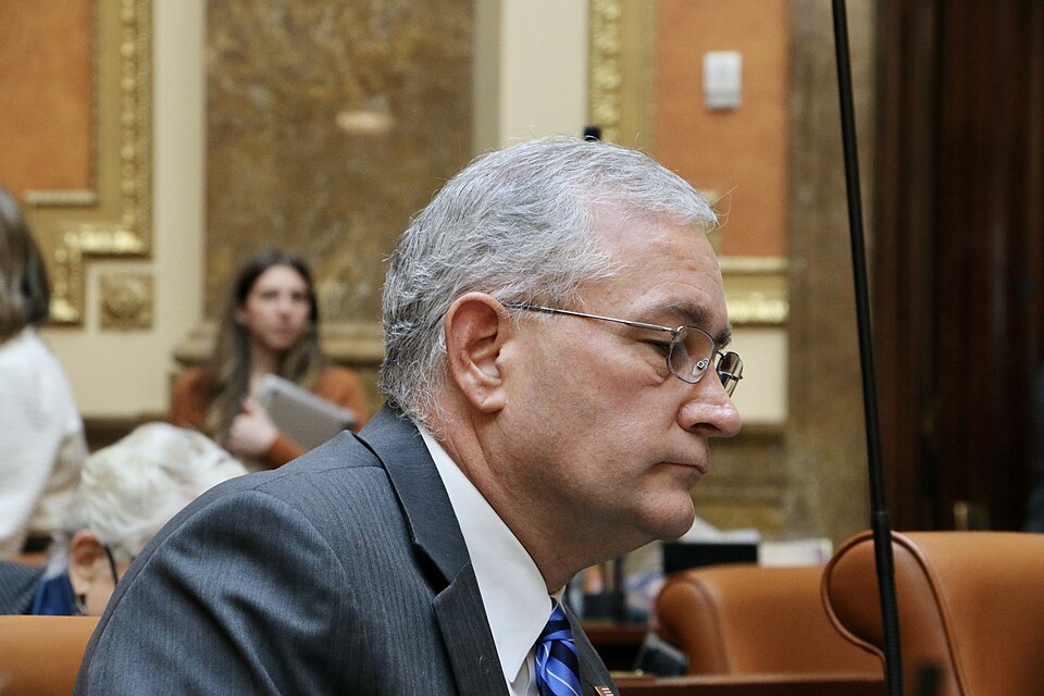 Nelson Abbott, wearing glasses and a dark suit, sits at a desk in the Utah House chamber.