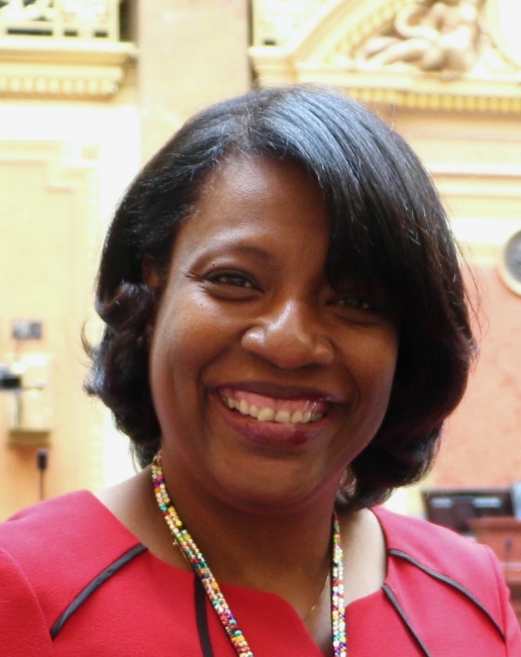 Sandra Hollins smiling in a red outfit in the House chamber.