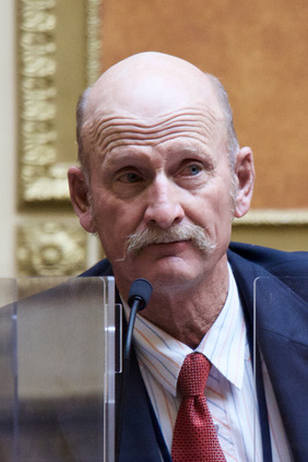 Scott Chew in a dark suit and red tie at a microphone.