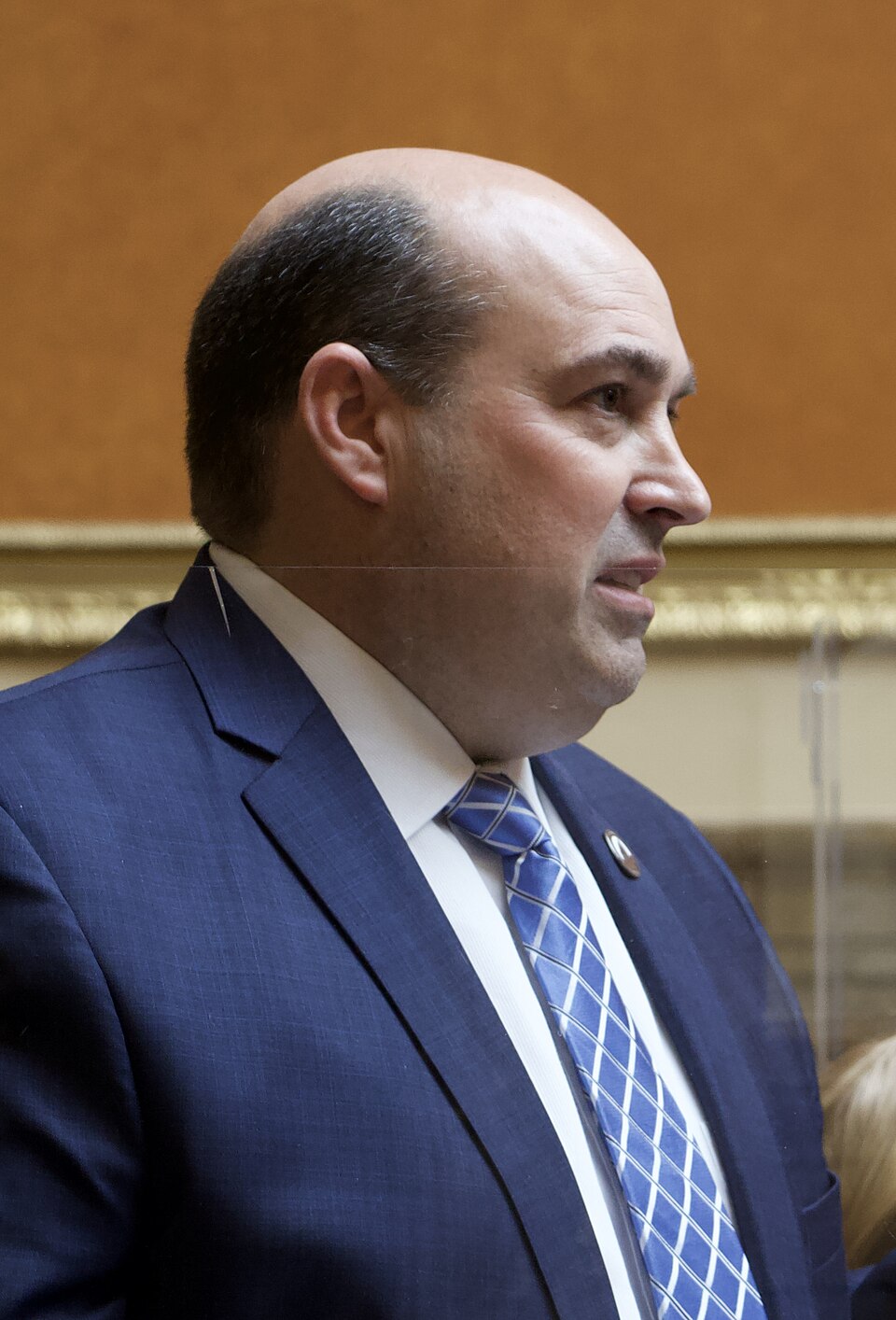 Walt Brooks in a blue suit and striped tie speaks in the Utah House chamber.