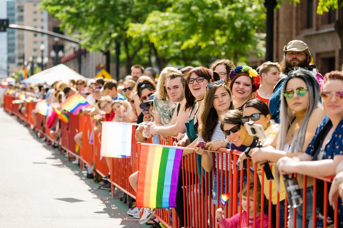Spectators with rainbow flags behind a parade barrier